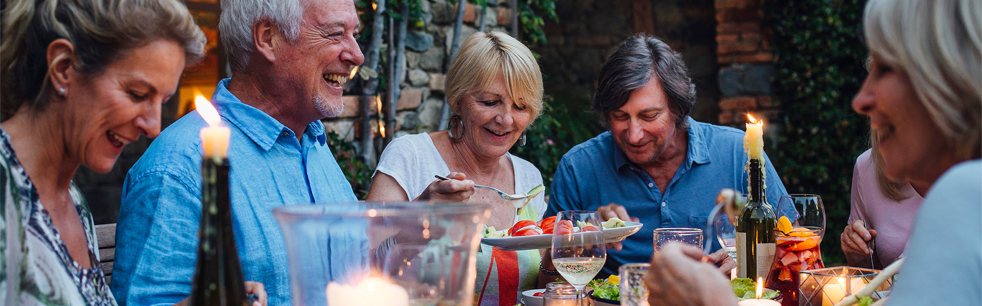 Flera äldre personer sitter runt ett middagsbord utomhus en sommarkväll